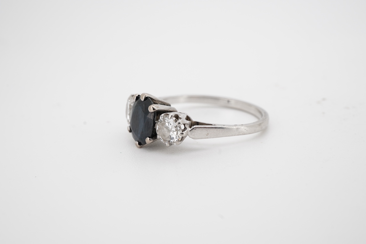 A white metal, single stone sapphire and two stone diamond set ring, the oval cut sapphire approx. 7mm by 5.8mm, the diamonds approx. 0.25ct each, size N.